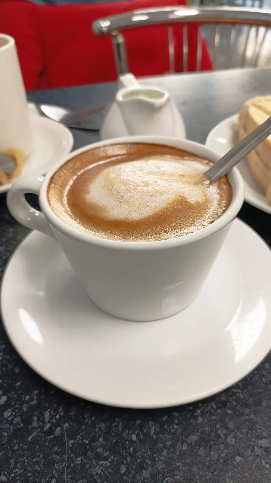 A frothy coffee in a white cup and saucer at Station Cafe